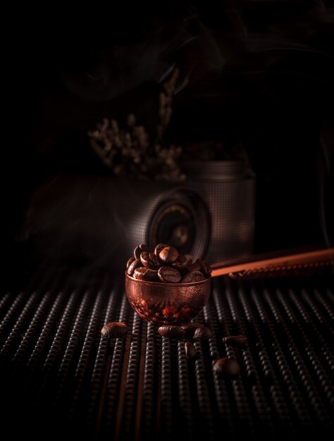 Geröstete Kaffeebohnen im Kupferlöffel mit Rauch auf dunklem Hintergrund. Der Geruch von aromatischem Kaffee am Morgen.