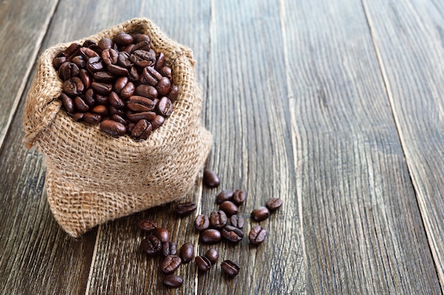 Geröstete Kaffeebohnen in einem Leinensack auf einem hölzernen Hintergrund. Platz kopieren. Kaffeeexportkonzept