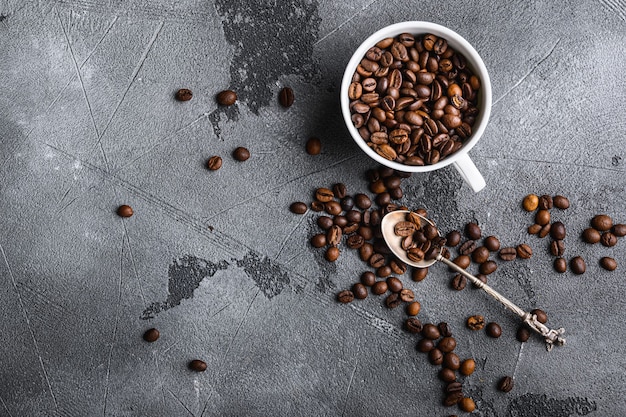 Geröstete Kaffeebohnen in einer Tasse auf grauem, flachem Boden mit Copyspace