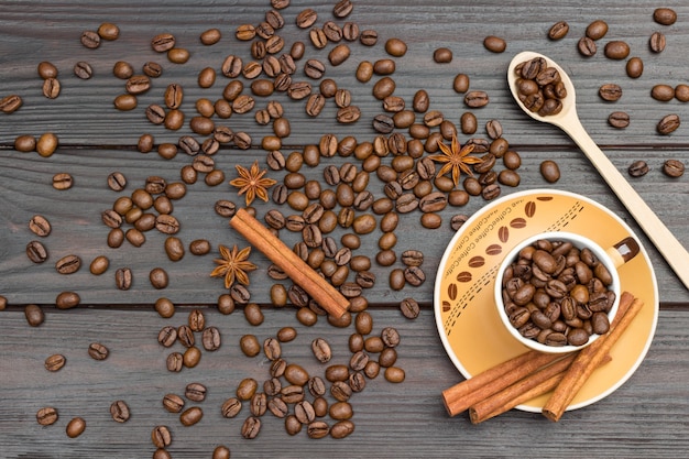 Geröstete Kaffeebohnen in Tasse und Holzlöffel. Zimtstangen auf Untertasse. Kaffeebohnen und Sternanis auf dem Tisch. Dunkler Holzhintergrund. Flach legen