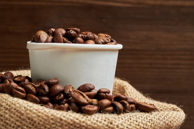 Geröstete Kaffeebohnen liegen in einem Pappbecher in einer Strickbeutel