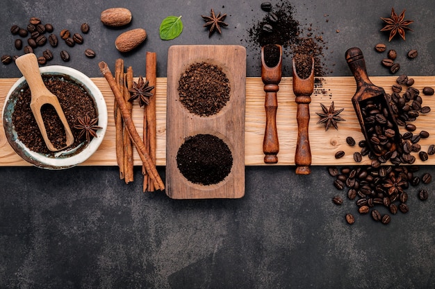 Geröstete Kaffeebohnen mit Kaffeepulver und geschmackvollen Zutaten für eine leckere Kaffeezubereitung auf dunklem Stein.