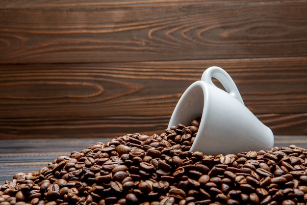 Geröstete Kaffeebohnen und Tasse auf hölzernem Hintergrund