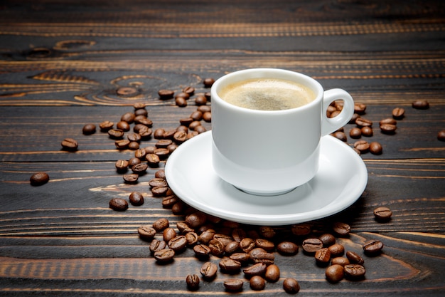 Geröstete Kaffeebohnen und Tasse auf hölzernem Hintergrund