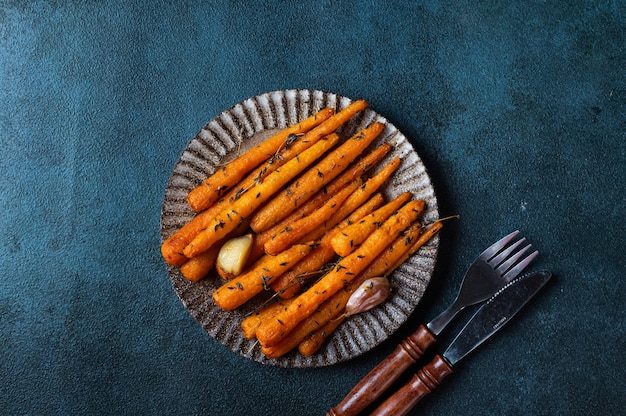 Geröstete Karotten verzehrfertig. Glasierte Karotte mit Kräuter- und Knoblauchdraufsicht. Gebratene Karotte auf dunklem Hintergrund. Gebratenes Gemüse. Komfort Essen. Nachhaltiger Konsum