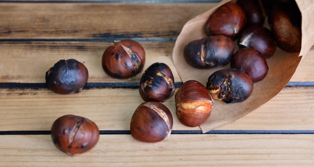 Geröstete Kastanien in einer Papiertüte auf Holztisch verschüttet