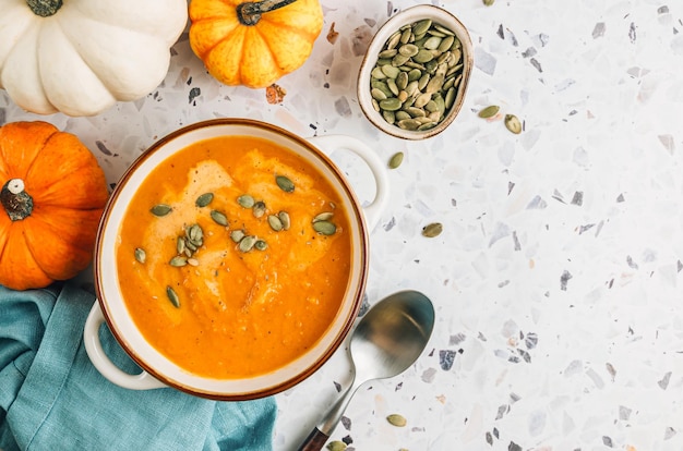 Geröstete Kürbis- und Karottensuppe mit Sahne und Kürbiskerne auf weißem Betongrund Top-Ansicht mit Kopierplatz