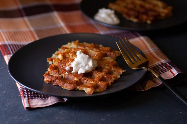 Geröstete Wiener Zucchini-Waffeln mit Sauerrahmsauce auf zwei schwarzen Tellern