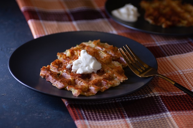 Geröstete Wiener Zucchini-Waffeln mit Sauerrahmsauce auf zwei schwarzen Tellern