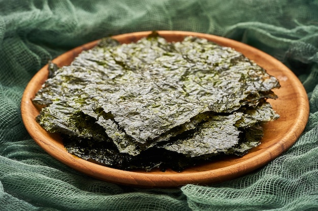 Foto gerösteter nori-laver-algen-snack in holzplatte auf grünem stoffhintergrund.