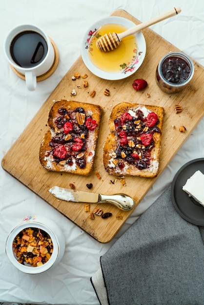 Geröstetes Brot mit Honig, Frischkäse, Marmelade mit roten Früchten und Kaffee