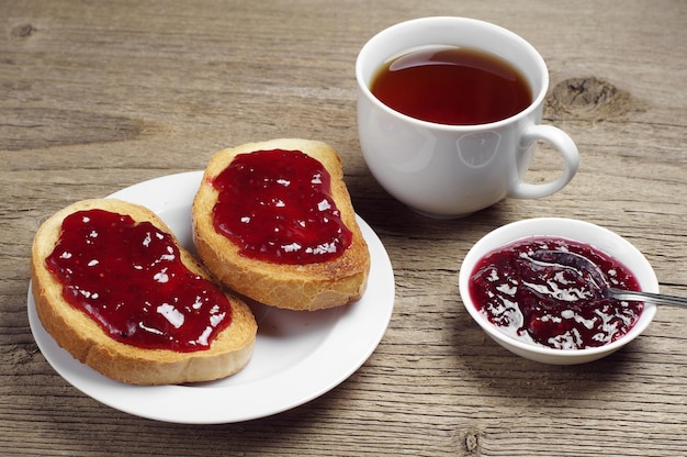 Geröstetes Brot mit Marmelade und Tasse Tee auf rustikalem Holztisch