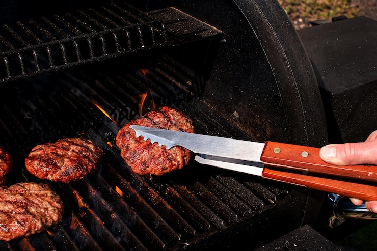 Foto geröstetes fleisch bbq burger patty für hamburger in zangen utensilien über flammendem grill grillrauch
