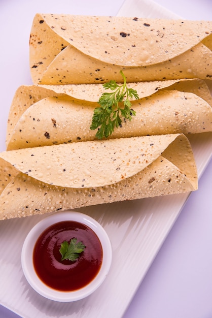 Geröstetes Rollpapad ist ein traditionelles indisches Gericht oder eine Beilage, das mit Tomatenketchup über einer bunten oder hölzernen Tischplatte serviert wird. Selektiver Fokus