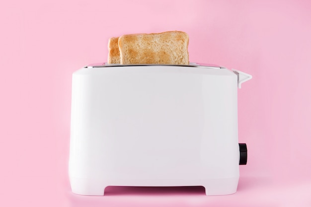 Geröstetes Toastbrot im weißen Toaster an der rosa Wand