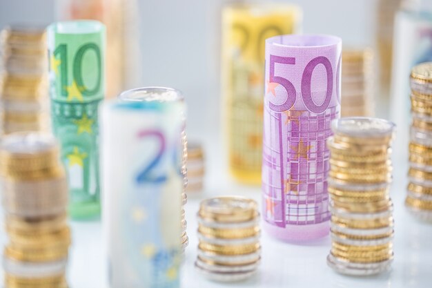 Gerollte Euro-Banknoten und Münzentürme in anderen Positionen gestapelt.