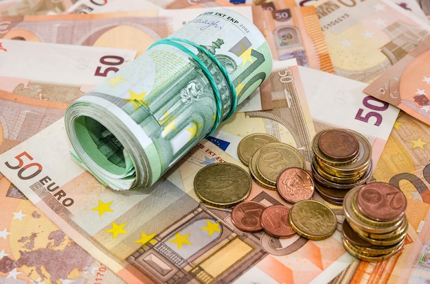 Foto gerollte hundert-euro-scheine und fünfzig-euro-scheine im hintergrund mit cent-stapeln