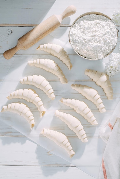 Gerollter Croissantteig und bereit zum Backen auf einem weißen Holztisch auf Backpapier in der Morgensonne