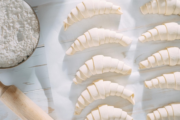 Foto gerollter croissantteig und bereit zum backen auf einem weißen holztisch auf backpapier in der morgensonne