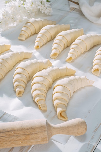 Gerollter Croissantteig und bereit zum Backen auf einem weißen Holztisch auf Backpapier in der Morgensonne