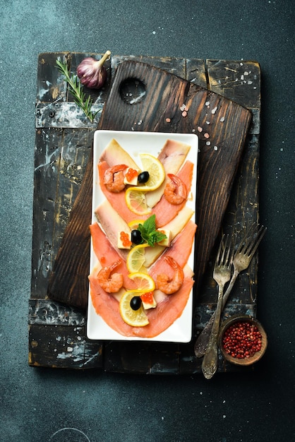 Gesalzene Lachs, Garnelen und Kaviar mit Butter und Zitrone Vorspeise Auf einem dunklen Stein-Hintergrund Freier Platz für Text