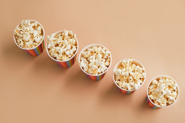 Gesalzenes Popcorn in kleinen gestreiften Pappbechern auf einer beigen Oberfläche
