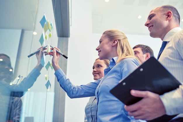 Foto geschäft, menschen, teamarbeit und planungskonzept - lächelndes geschäftsteam mit markern und aufklebern, die im büro arbeiten