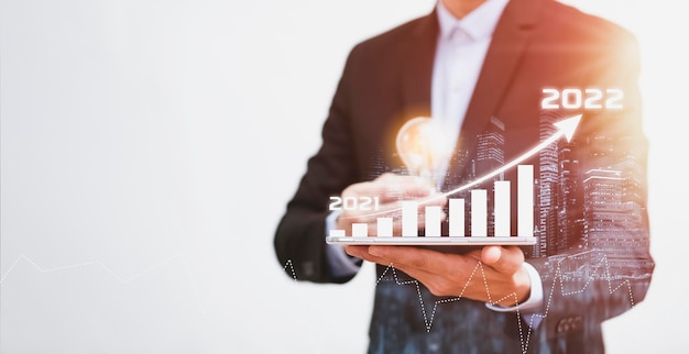 Geschäft mit Glühbirne mit Wachstumsdatendiagrammpfeil mit Diagramm 2022-Budget, Geschäftsmann, der auf das zukünftige Wachstumsjahr 2021 bis 2022 des Unternehmens mit Pfeildiagramm zeigt, Entwicklung zum Erfolg und zur Motivation.