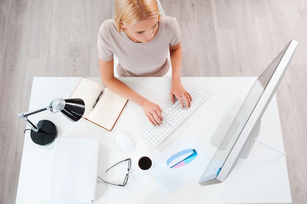 Geschäft zuerst. Draufsicht einer schönen jungen blonden Frau, die am Computer arbeitet, während sie an ihrem Arbeitsplatz sitzt working