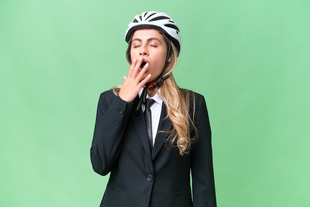Geschäftliche uruguayische Frau, die einen Helm trägt, Biker vor isoliertem Hintergrund, der gähnt und den weit geöffneten Mund mit der Hand bedeckt