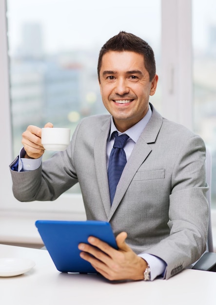 Geschäfts-, Bildungs-, Menschen- und Technologiekonzept - lächelnder Geschäftsmann mit Tablet-PC-Computer und Kaffee im Büro