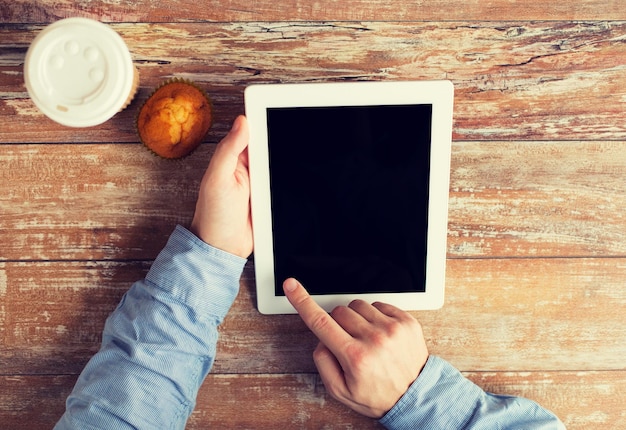 Foto geschäfts-, bildungs-, menschen- und technologiekonzept - nahaufnahme männlicher hände mit tablet-pc-computer, muffin und kaffeetasse auf dem tisch