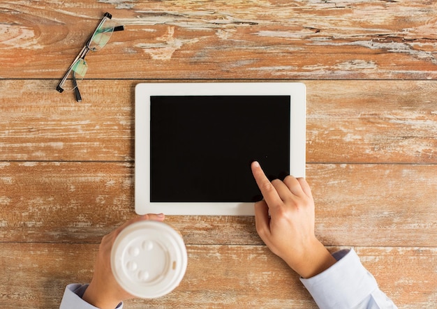 Foto geschäfts-, bildungs-, menschen- und technologiekonzept - nahaufnahme weiblicher hände, die mit dem finger auf den schwarzen leeren bildschirm des tablet-pc-computers mit kaffeetasse und brille zeigen