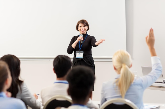 Geschäfts-, Bildungs- und Menschenkonzept - lächelnde Geschäftsfrau oder Lehrerin mit Mikrofon, die bei einer Konferenzpräsentation oder einem Vortrag Fragen beantwortet