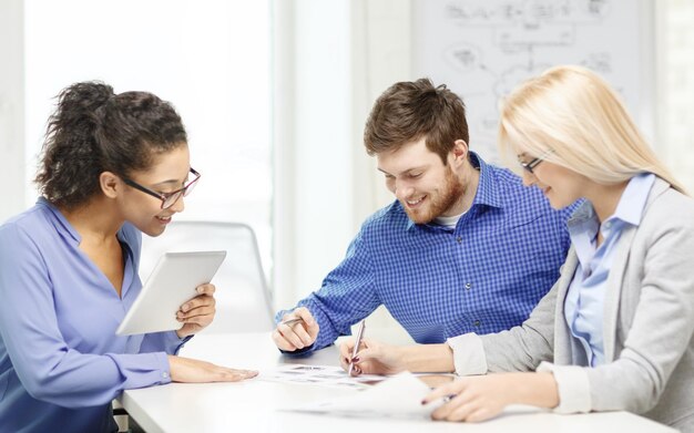 geschäfts-, büro- und startkonzept - lächelndes kreatives team mit tisch-pc-computern und papieren, die im büro arbeiten