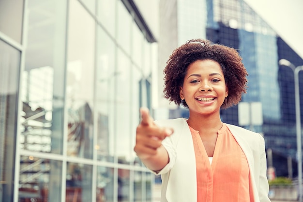 Geschäfts-, Gesten- und Personenkonzept - junge lächelnde afroamerikanische Geschäftsfrau in der Stadt, die mit dem Finger auf Sie zeigt