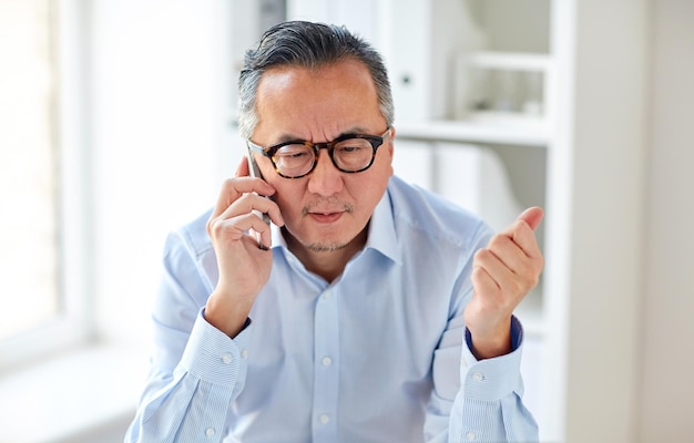 Geschäfts-, Menschen-, Kommunikations- und Technologiekonzept - seriöser asiatischer Geschäftsmann, der im Büro sein Smartphone anruft