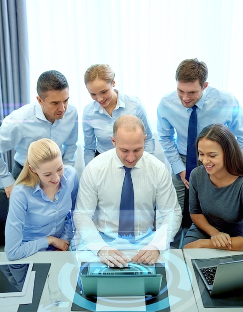 Geschäfts-, Menschen-, Technologie- und Teamwork-Konzept - lächelndes Geschäftsteam mit Laptop-Computer und virtueller Projektion, das im Büro arbeitet