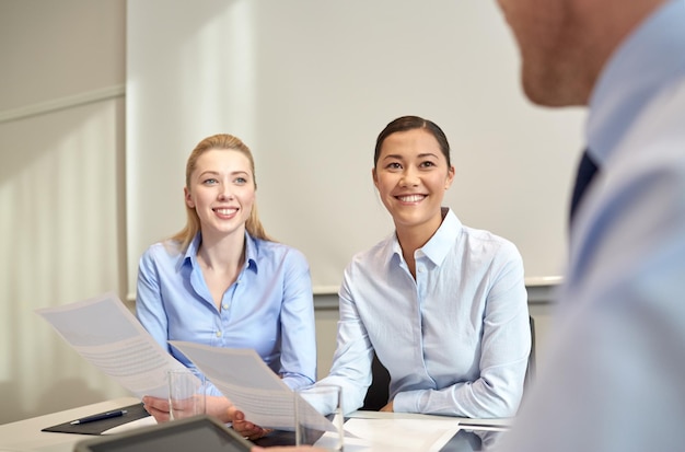 Geschäfts-, Menschen- und Teamwork-Konzept - lächelnde Geschäftsfrauen, die sich im Büro treffen