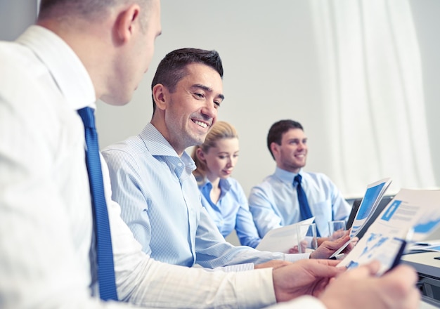 Geschäfts-, Menschen- und Technologiekonzept - lächelndes Geschäftsteam mit Laptop-Computer, Papieren und Smartphone-Meeting im Büro