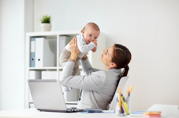 Geschäfts-, Mutterschafts-, Multitasking-, Familien- und Personenkonzept – glücklich lächelnde Geschäftsfrau mit Baby und Laptop-Computer, die im Büro arbeitet