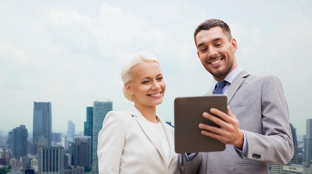 Geschäfts-, Partnerschafts-, Technologie- und Personenkonzept - lächelnder Geschäftsmann und Geschäftsfrau mit Tablet-PC-Computer über Stadthintergrund