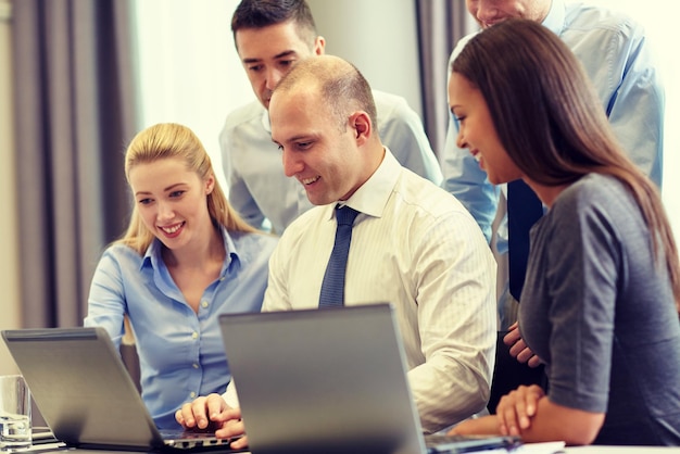 Geschäfts-, Personen- und Technologiekonzept - lächelndes Geschäftsteam mit Laptop-Computern, die sich im Büro treffen