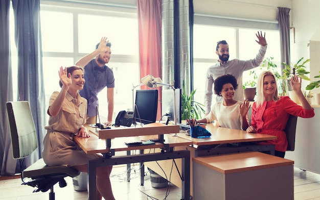 geschäfts-, start- und bürokonzept - fröhliches kreatives team winkt im büro