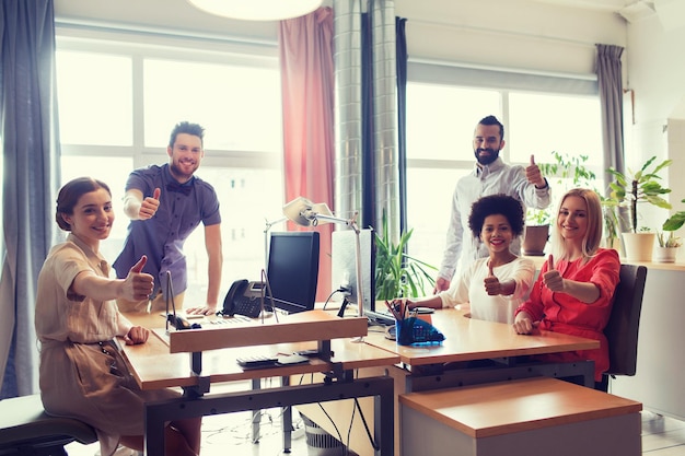 geschäfts-, start- und personenkonzept - glückliches kreatives team, das im büro daumen hoch zeigt