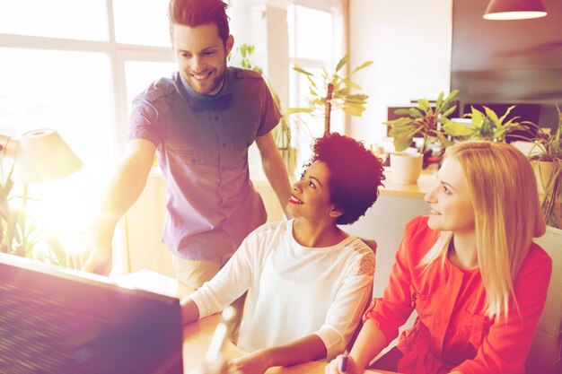 Foto geschäfts-, start- und personenkonzept - glückliches kreatives team, das mit computer im büro vernetzt