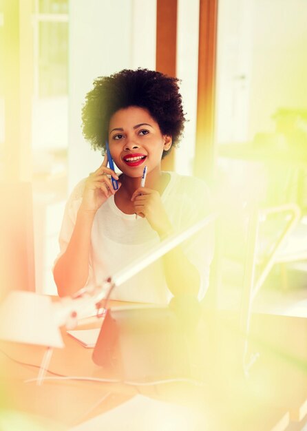 Geschäfts-, Startup- und People-Konzept - glückliche afroamerikanische Geschäftsfrau oder Kreativarbeiterin, die im Büro Smartphone anruft