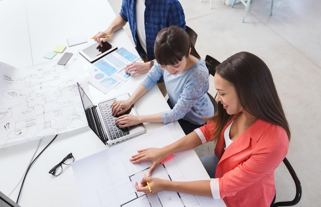 Geschäfts-, Startup- und People-Konzept - glückliches Kreativteam mit Laptop und Blaupause im Büro