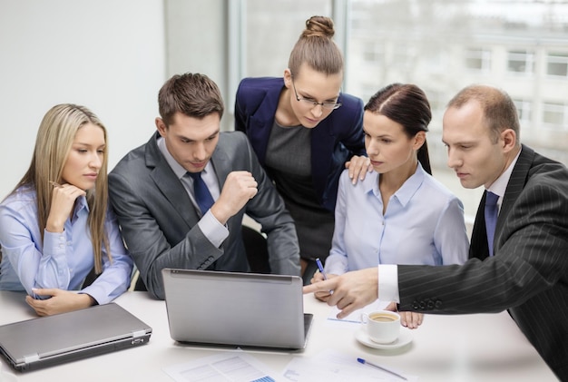 geschäfts-, technologie- und bürokonzept - seriöses geschäftsteam mit laptops, dokumenten und kaffee, das im büro diskutiert