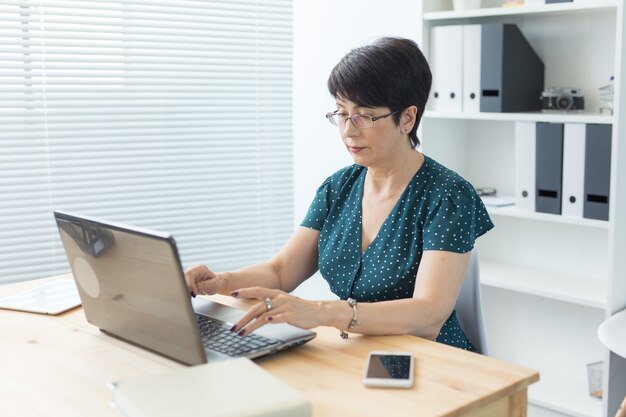 Geschäfts-, Technologie- und Personenkonzept - Frau mittleren Alters arbeitet im Büro und benutzt einen Laptop